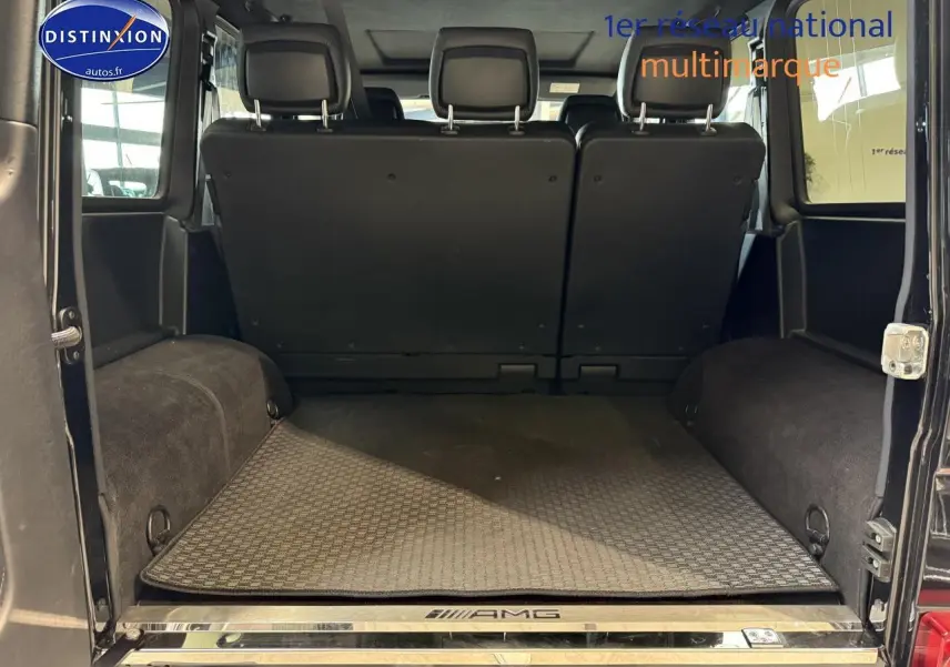 Coffre ouvert vu de l'arrière d'un Mercedes Classe G 5.5 63 AMG noir avec tapis AMG et banquette arrière relevée.