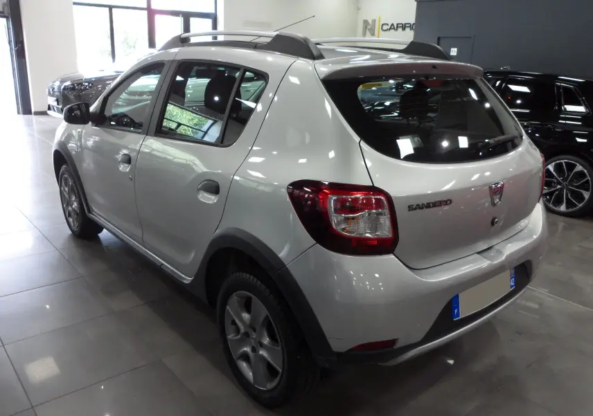 Vue 3/4 arrière droite d'une Dacia Sandero Stepway gris platine en intérieur, avec barres de toit et jantes alliage.
