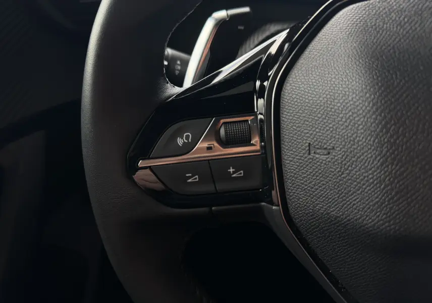 Gros plan sur les commandes gauche du volant noir du Peugeot 2008 2023, boutons de volume et téléphone visibles.