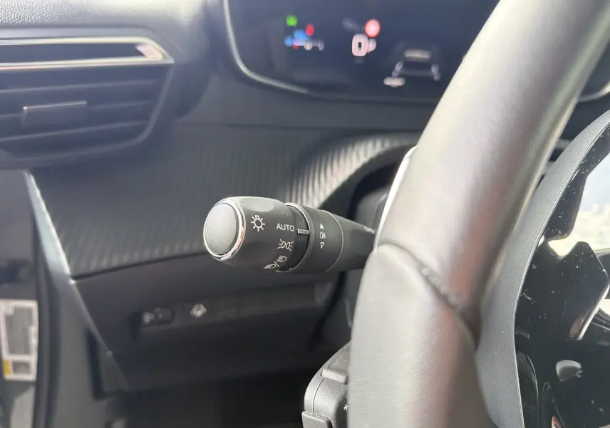 Gros plan sur la commande des feux à gauche du volant dans l’habitacle gris du Peugeot 2008 1.2 130 EAT8 Allure 2023.