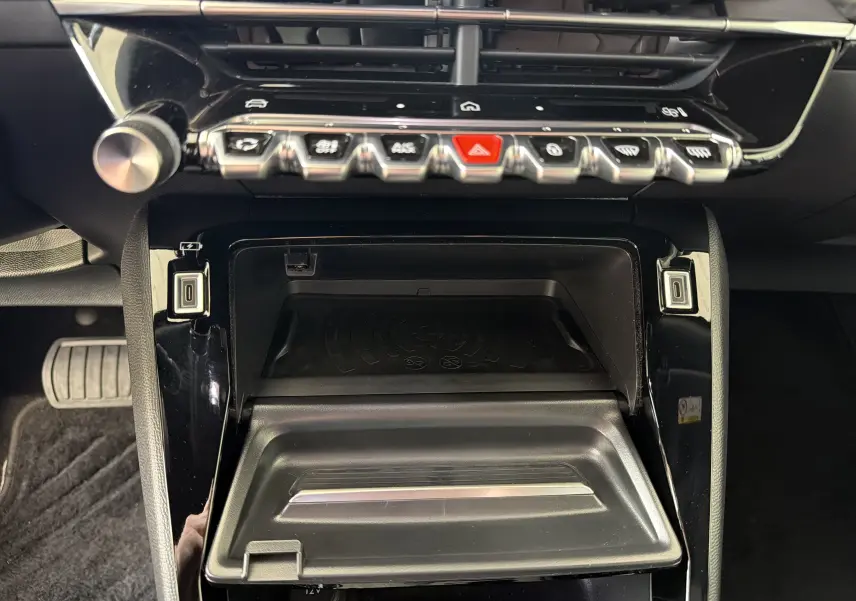 Gros plan sur la console centrale noire brillante du Peugeot 2008 2023, montrant les commandes et un espace de rangement ouvert.