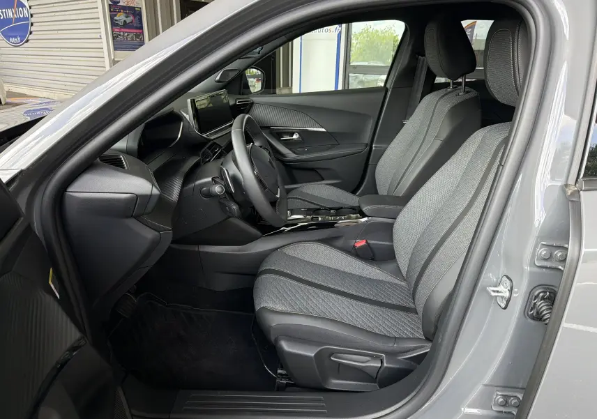 Vue intérieure côté conducteur de la Peugeot 2008 gris Sellenium, montrant les sièges tissu et la planche de bord moderne.
