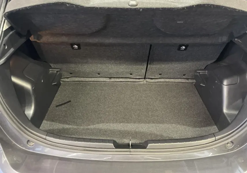 Coffre ouvert vu de l'arrière d'une Toyota Yaris hybride gris foncé métallisé, intérieur du coffre en tissu gris.