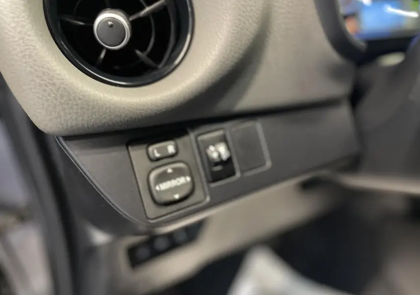 Détail du tableau de bord côté gauche avec commandes de réglage des rétroviseurs dans une Toyota Yaris hybride gris foncé.
