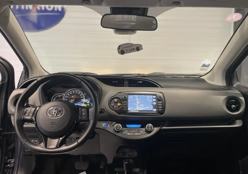 Vue frontale de l'intérieur de la Toyota Yaris hybride 2020 avec tableau de bord noir et écran tactile de navigation.