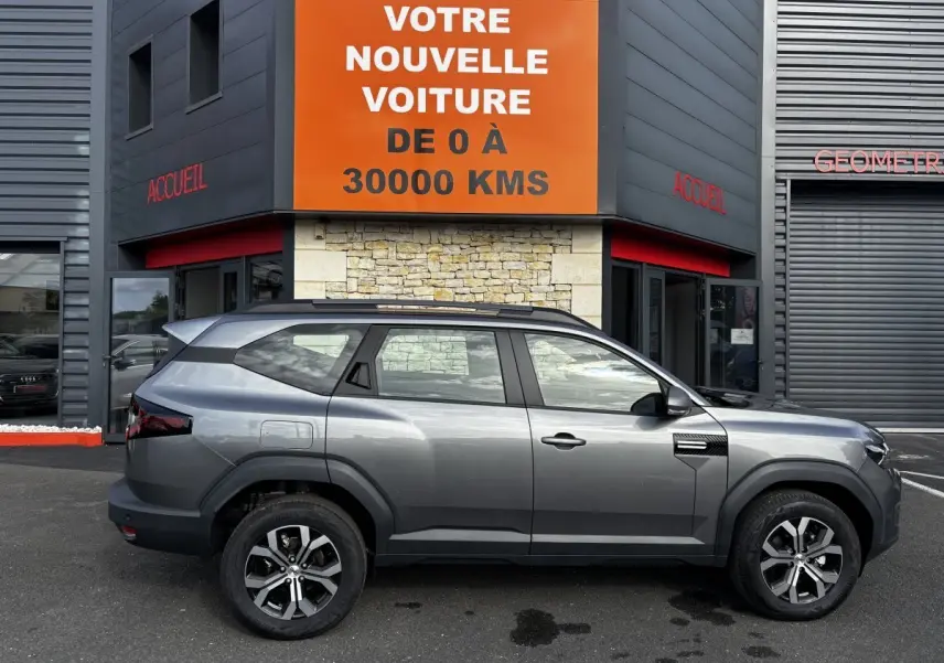 Profil droit du Dacia Bigster gris foncé 2025 avec jantes alliage et barres de toit noires visibles.
