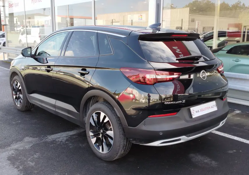 Vue 3/4 arrière droite d’un Opel Grandland X noir diamant avec jantes bi-ton et vitres teintées, stationné devant un showroom.