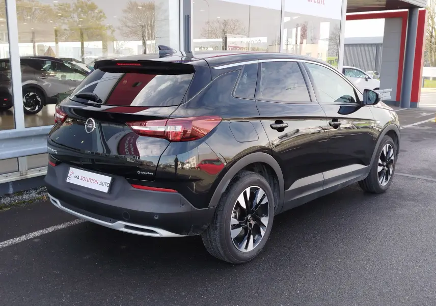 Vue 3/4 arrière droite d’un Opel Grandland X noir diamant avec jantes bi-ton et vitres teintées, stationné devant un showroom.