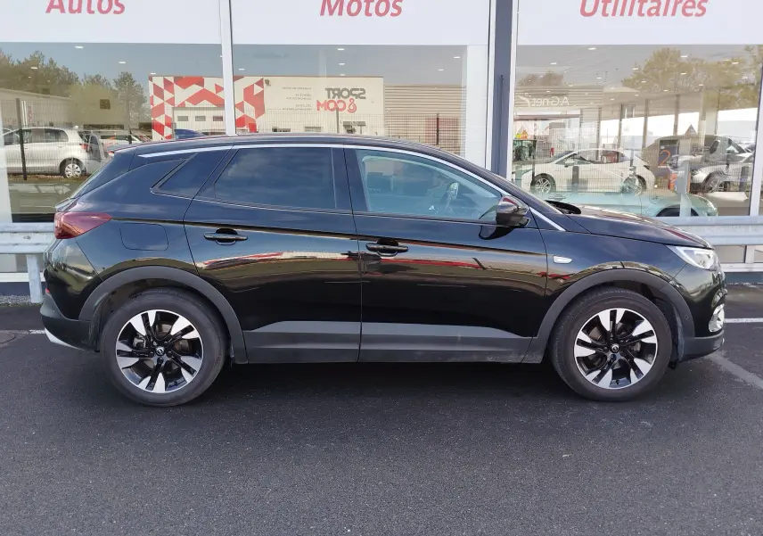 Vue de profil côté gauche d’un Opel Grandland X noir diamant avec jantes bi-ton et vitres teintées, stationné devant un showroom.
