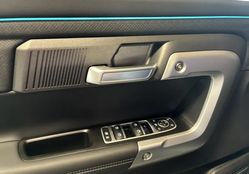Gros plan sur la porte intérieure côté conducteur du JAECOO J7 gris olive, avec commandes électriques et poignée argentée.