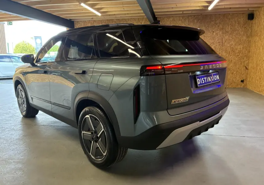 SUV JAECOO J7 gris olive vu en 3/4 arrière droit, toit noir et feux arrière LED allumés dans un garage.