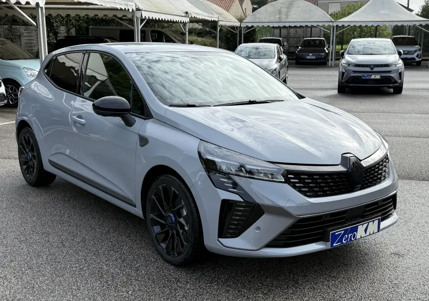 Renault Clio V 1.6 E-TECH gris Rafale vue 3/4 avant droit, avec jantes noires et calandre noire distinctive.