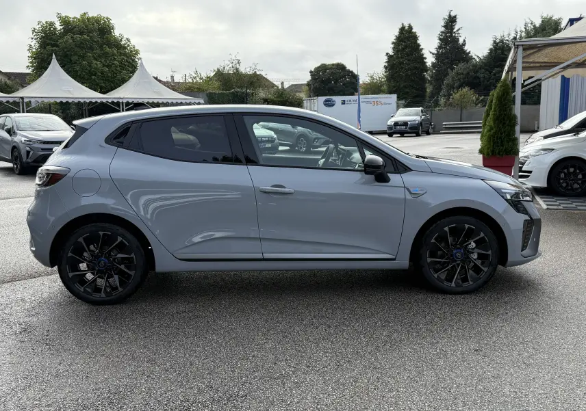 Profil latéral droit d'une Renault Clio V 1.6 E-TECH gris rafale avec jantes noires et vitres teintées, en extérieur.