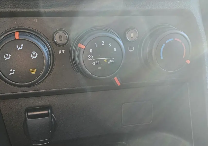 Gros plan sur les commandes de climatisation manuelle du tableau de bord d’une Dacia Sandero III blanche.
