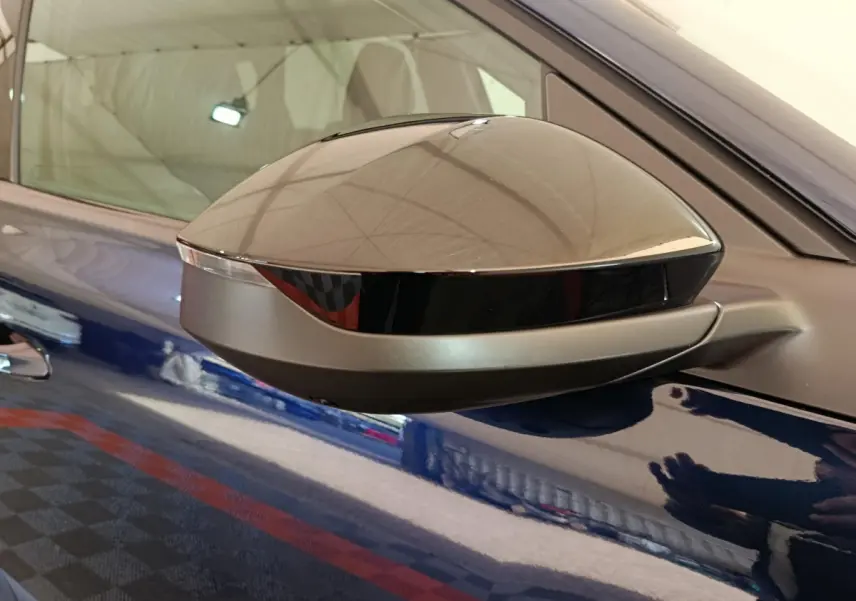 Gros plan sur le rétroviseur droit noir brillant d'une Citroën C5 hybride bleu, reflet du plafond et d'une personne visible.