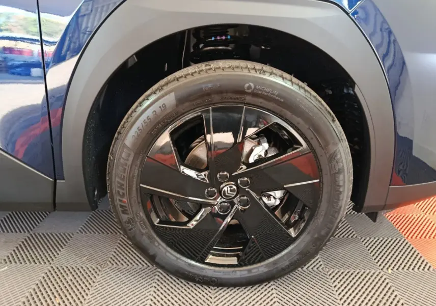 Gros plan sur la roue avant droite noire brillante d’un Citroën C5 Hybride bleu, avec jante au design moderne.