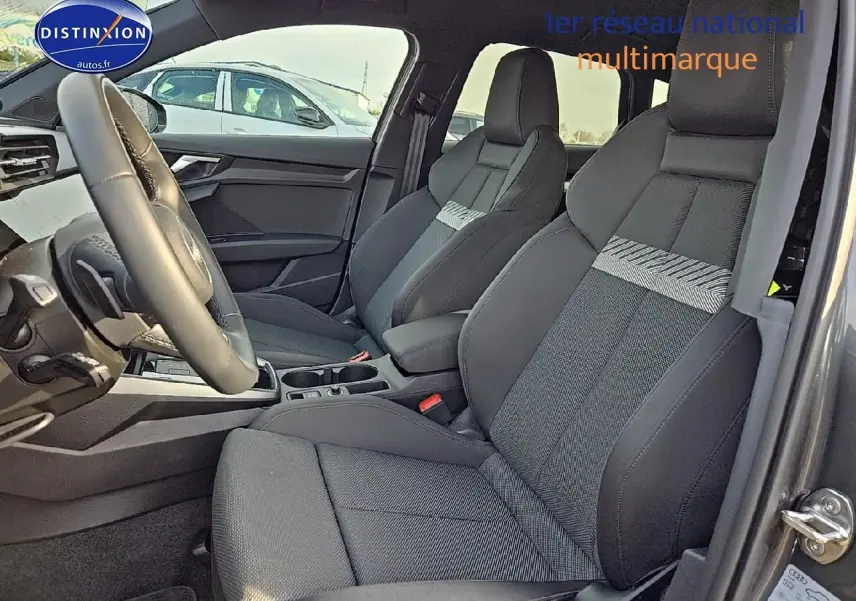 Intérieur avant de l'Audi A3 Sportback 2024 avec sièges sport gris et volant cuir multifonction visible côté conducteur.