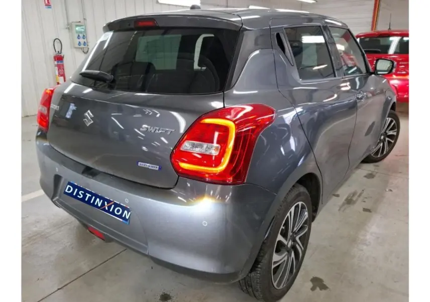 Vue 3/4 arrière droite d'une Suzuki Swift 1.2 Dualjet Hybrid grise de 2023 avec feux arrière allumés en intérieur.