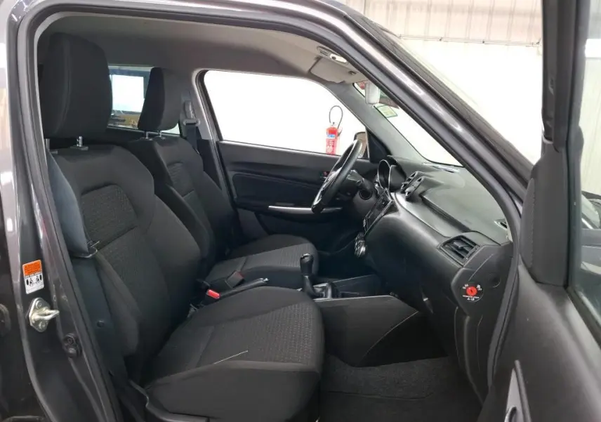 Vue intérieure côté conducteur de la Suzuki Swift grise 2023, montrant les sièges avant et le tableau de bord noir.