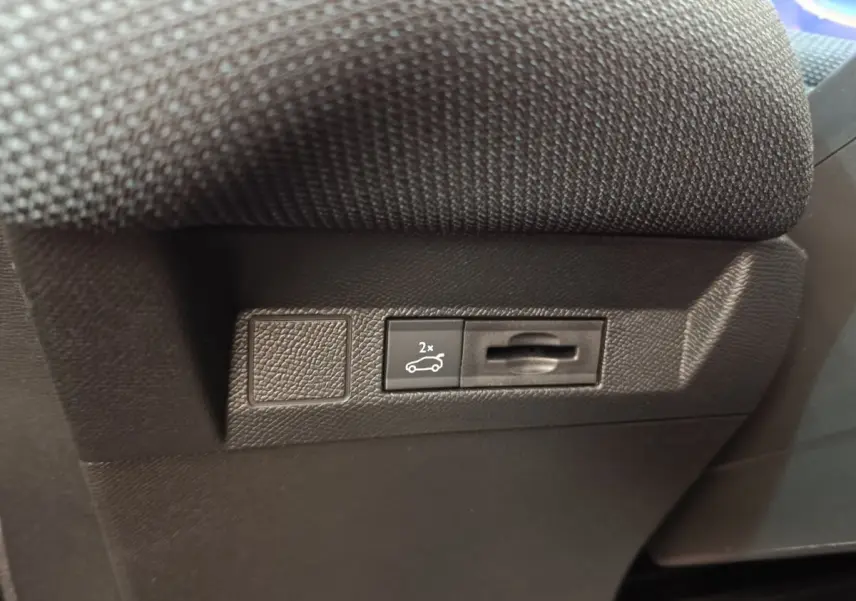 Gros plan sur la commande d'ouverture du coffre noir dans l'habitacle d'une Citroën C5 hybride verte.
