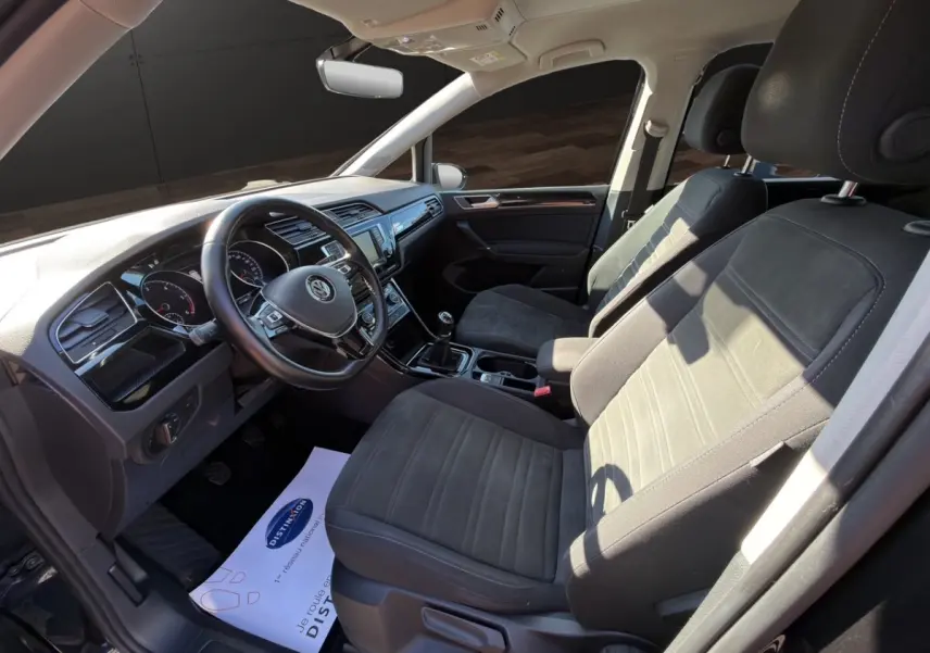 Vue intérieure côté conducteur du Volkswagen Touran 1.6 TDI noir, volant cuir alu multifonctions et boîte manuelle visible.