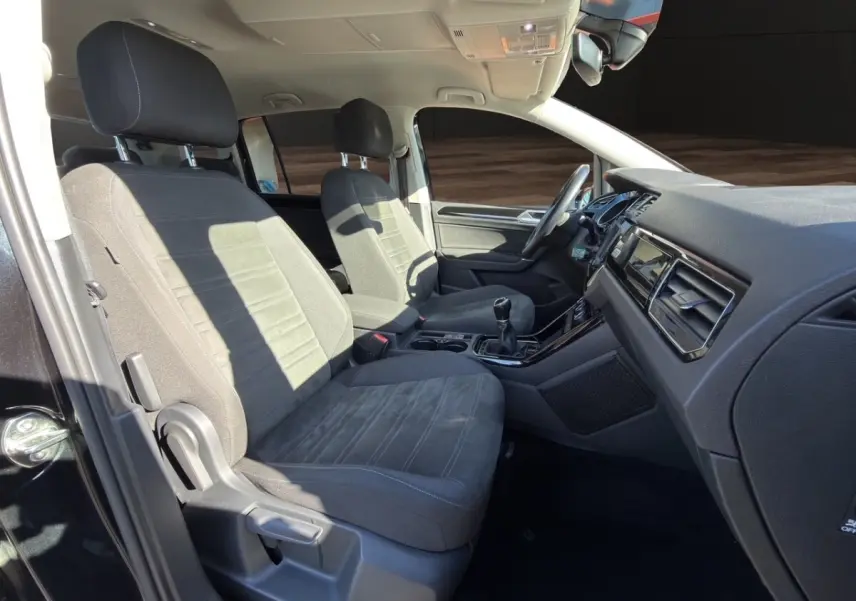 Intérieur avant du Volkswagen Touran noir 2016, sièges tissu gris, volant multifonctions et boîte manuelle visible.