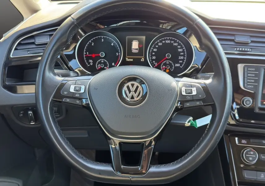Vue intérieure centrée sur le volant cuir et alu noir du Volkswagen Touran 2016 avec tableau de bord et commandes visibles.