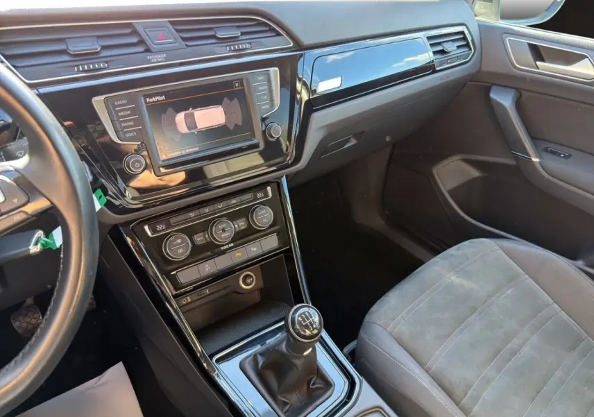 Intérieur avant droit du Volkswagen Touran noir 2016, avec tableau de bord, écran tactile et levier de vitesse manuel visible.