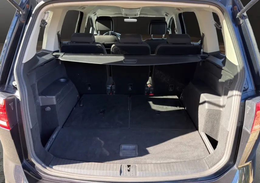 Coffre ouvert vu de l'arrière d'un Volkswagen Touran noir, montrant les sièges rabattus et la tablette de coffre.
