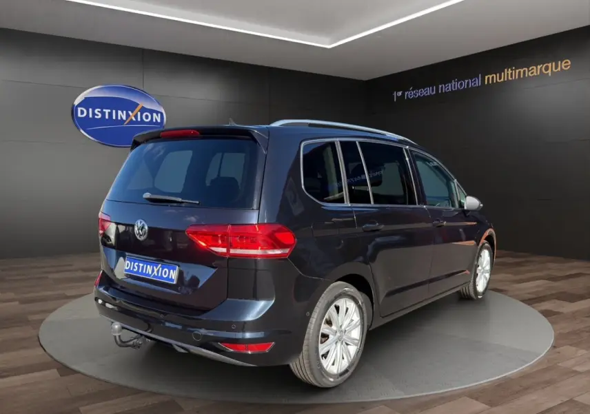 Volkswagen Touran noir vue 3/4 arrière droit avec attelage, en intérieur sur plateforme rotative.