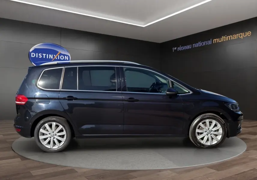 Profil droit d’un Volkswagen Touran noir 2016 avec jantes alliage et barres de toit chromées en showroom.