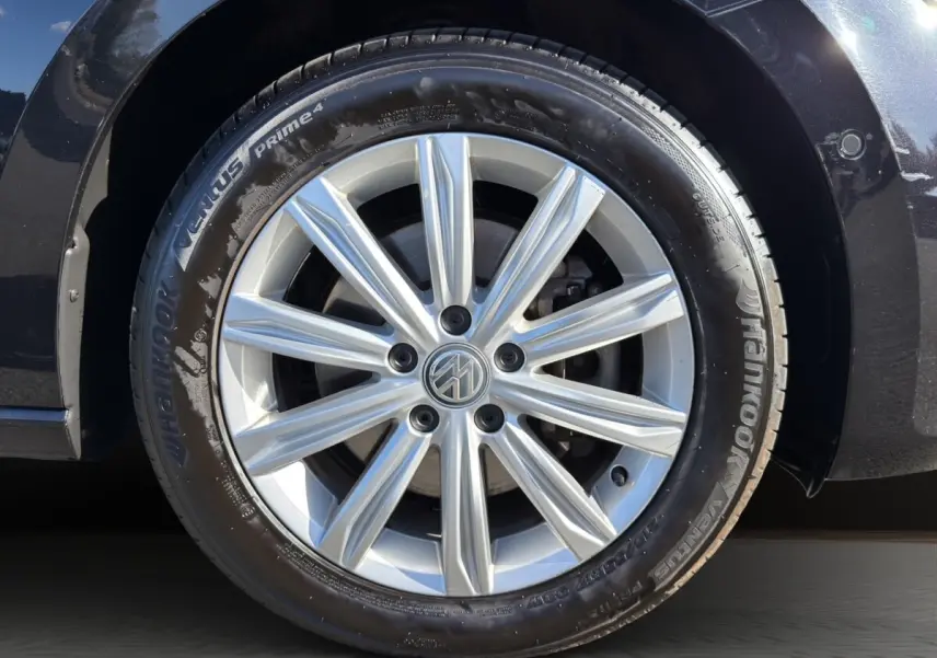 Gros plan sur la roue avant droite d’un Volkswagen Touran noir, avec jante alliage argentée à dix branches.