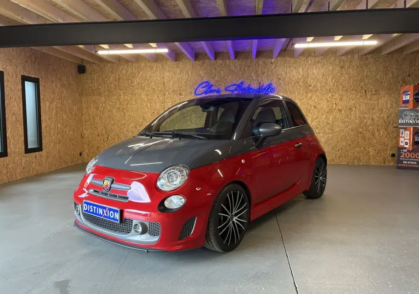 Vue 3/4 avant droite de l'Abarth 500 rouge avec capot noir et jantes noires à rayons fins dans un showroom.