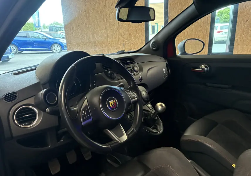 Intérieur côté conducteur de l'Abarth 500 rouge 2016, volant sport avec logo Abarth et levier de vitesses manuel visible.