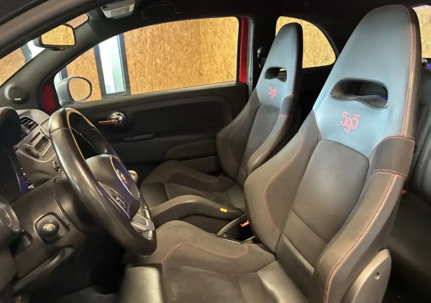 Vue intérieure côté conducteur de l'Abarth 500 rouge 2016 avec sièges sport noirs brodés "595" en rouge.