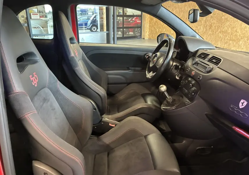 Intérieur de l'Abarth 500 rouge vu côté conducteur, sièges sport noirs avec surpiqûres rouges et logo 595 brodé.