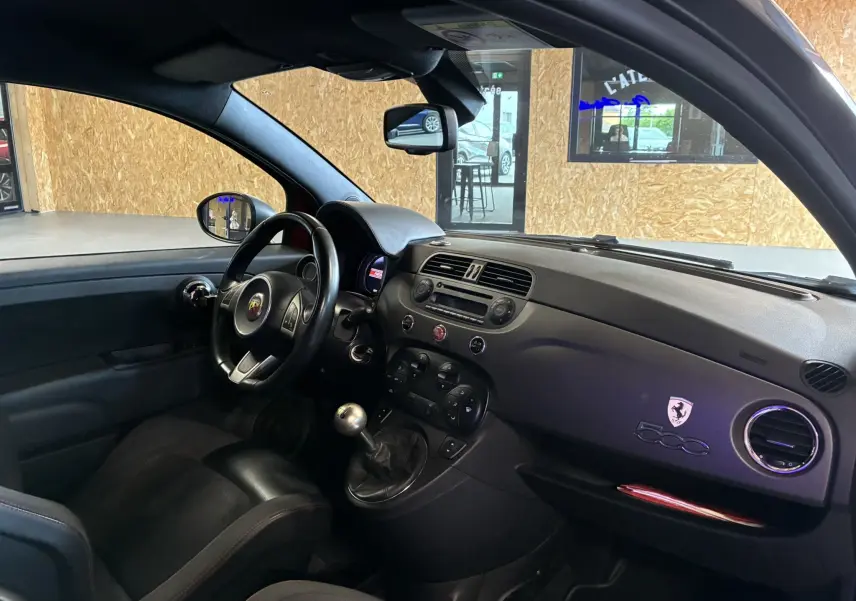 Vue intérieure côté conducteur de l'Abarth 500 rouge 2016, mettant en valeur le volant sport et la boîte manuelle.