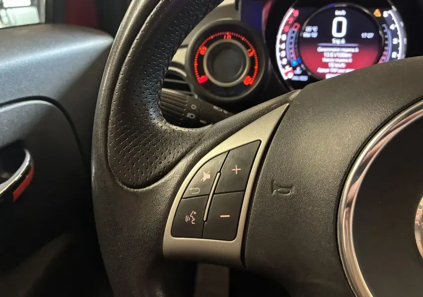 Gros plan sur le volant en cuir noir de l'Abarth 500 rouge 2016, avec commandes audio intégrées et tableau de bord lumineux.