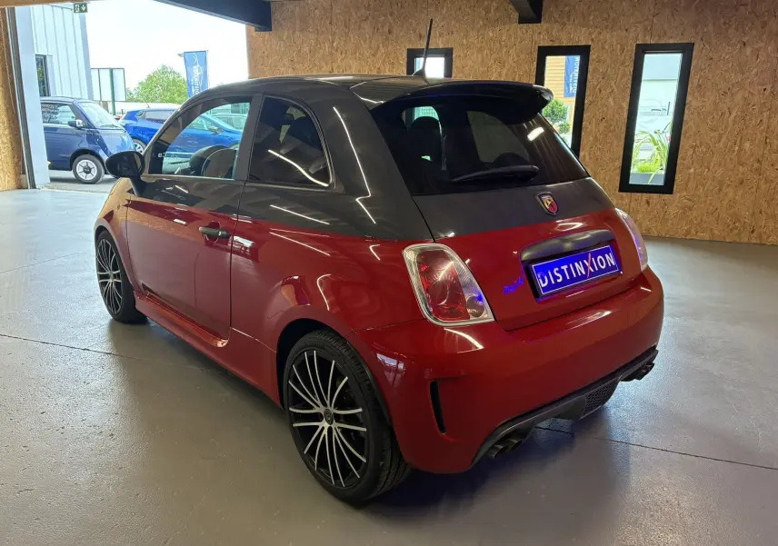 Vue 3/4 arrière droite d'une ABARTH 500 rouge avec toit noir et jantes alliage noires en intérieur showroom.