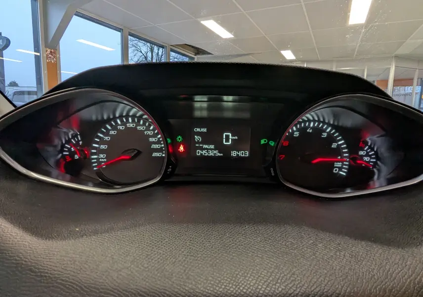 Vue rapprochée du tableau de bord de la Peugeot 308 noire, affichant le compteur de vitesse et le compte-tours allumés.