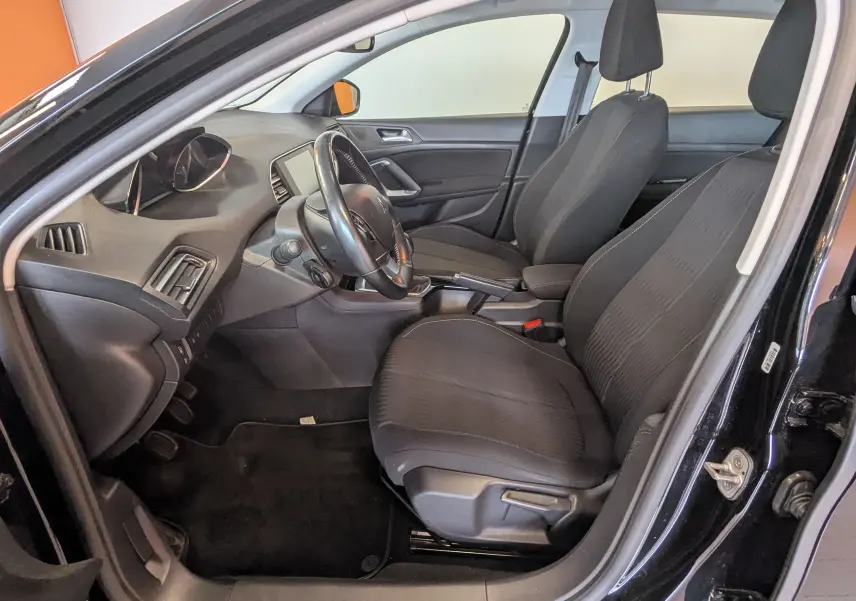 Vue intérieure côté conducteur de la Peugeot 308 noire de 2017, montrant les sièges en tissu gris et le tableau de bord.