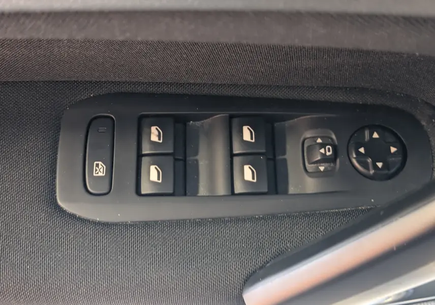 Gros plan sur les commandes de lève-vitres et réglages des rétroviseurs côté conducteur d’une Peugeot 308 noire.