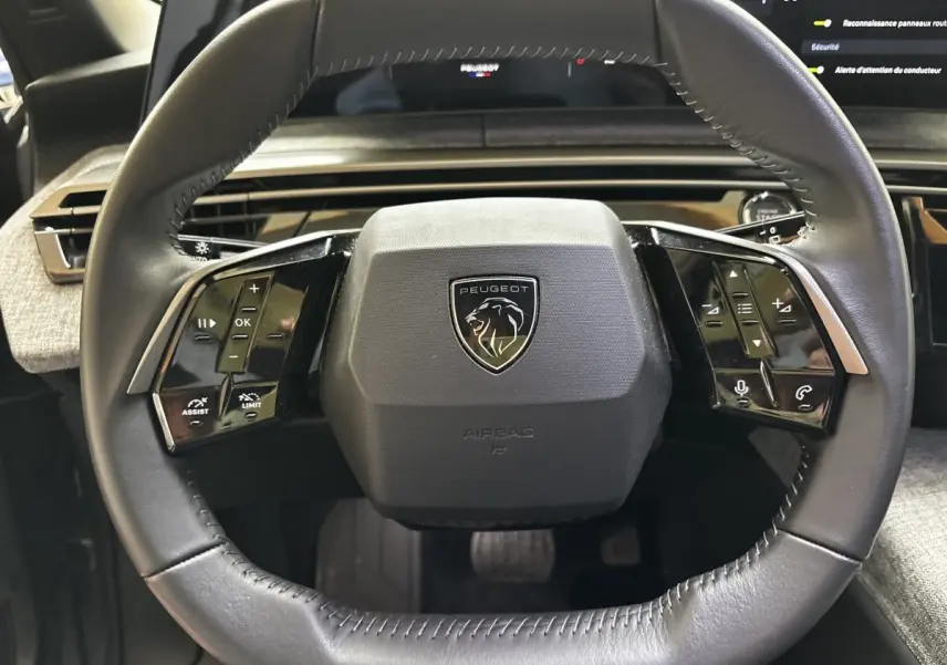 Gros plan sur le volant cuir noir du Peugeot 5008 2025 avec commandes multifonctions et logo lion central.
