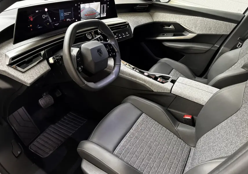 Vue intérieure côté conducteur du Peugeot 5008 2025, avec tableau de bord numérique et sièges gris clair tissu et cuir.