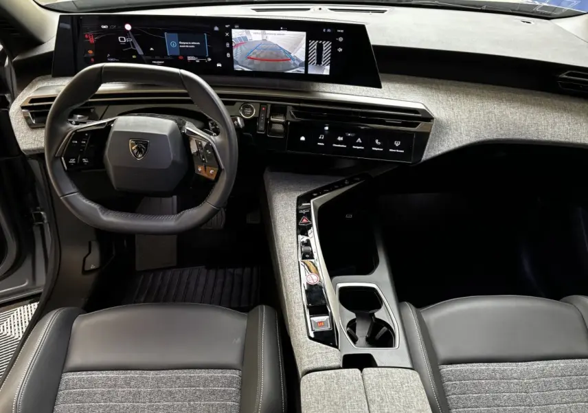 Vue intérieure avant du Peugeot 5008 2025 gris clair, tableau de bord avec écran tactile panoramique et volant multifonctions.