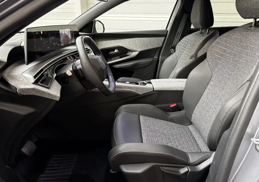 Vue intérieure côté conducteur de la Peugeot 5008 1.2 Hybrid 136 GT avec sièges tissu gris et cuir noir, tableau de bord moderne.