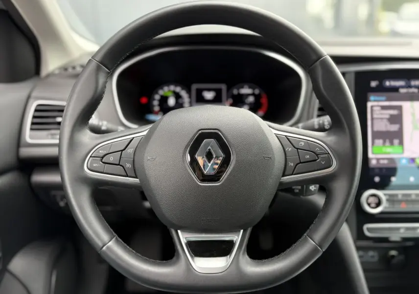 Volant en similicuir noir avec logo Renault au centre, tableau de bord numérique et écran tactile GPS à droite.