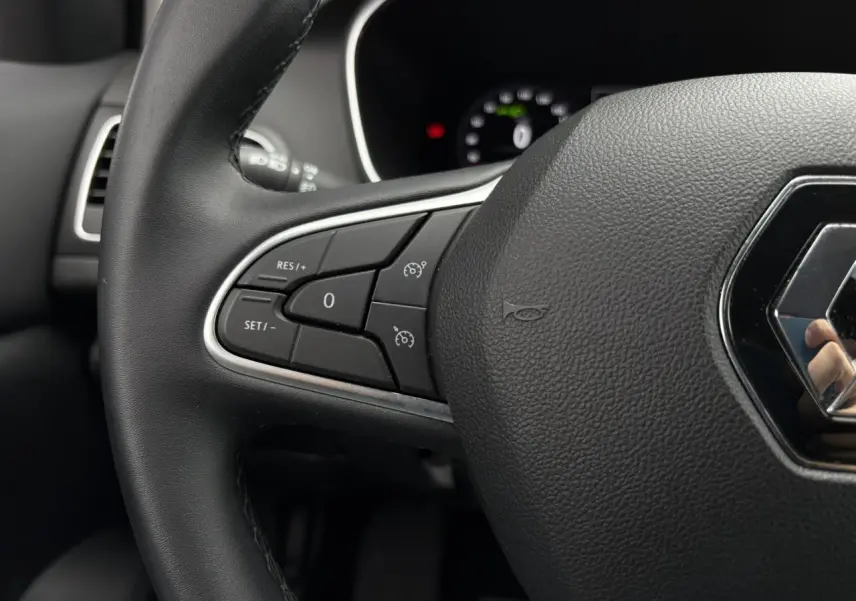Gros plan sur le volant noir de la Renault Mégane Break 2024 avec commandes de régulateur et logo Renault central.