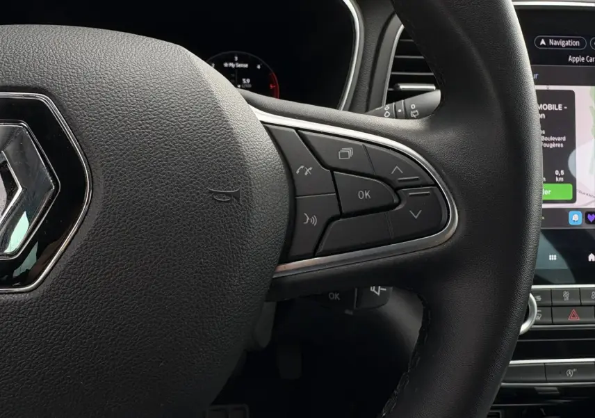 Gros plan sur le volant en similicuir noir de la Renault Mégane Break 2024 avec commandes multifonctions et écran tactile GPS visible.