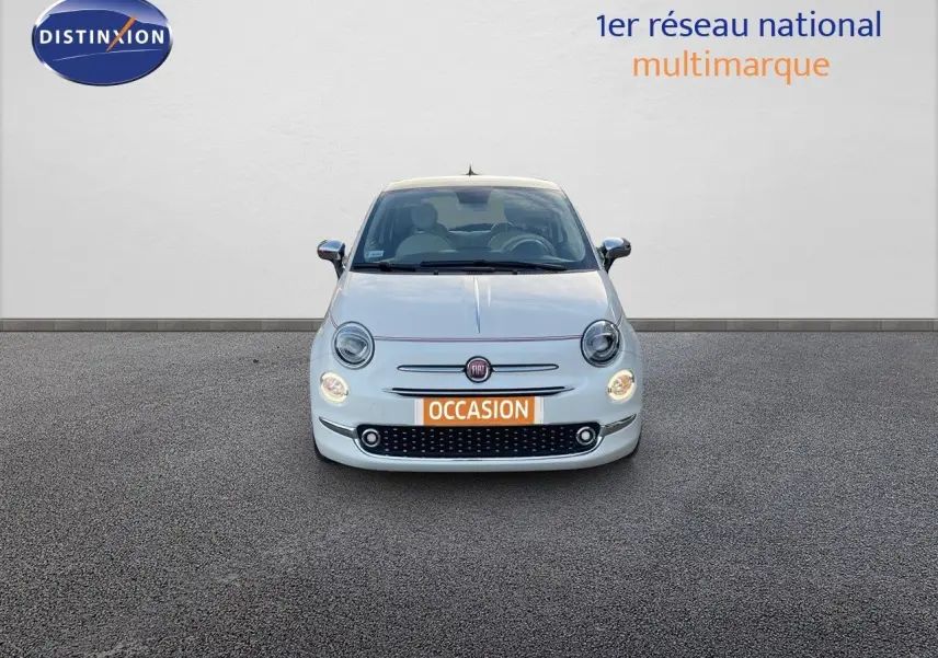 Vue frontale d'une Fiat 500 blanche 1.0 Hybrid 70ch DolceVita avec phares allumés et plaque occasion.